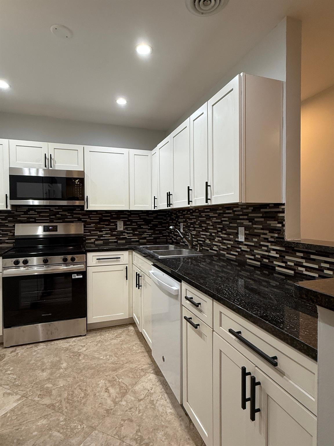 Kitchen with white cabinets, dark granite counters, mosaic backsplash, and stainless steel range.