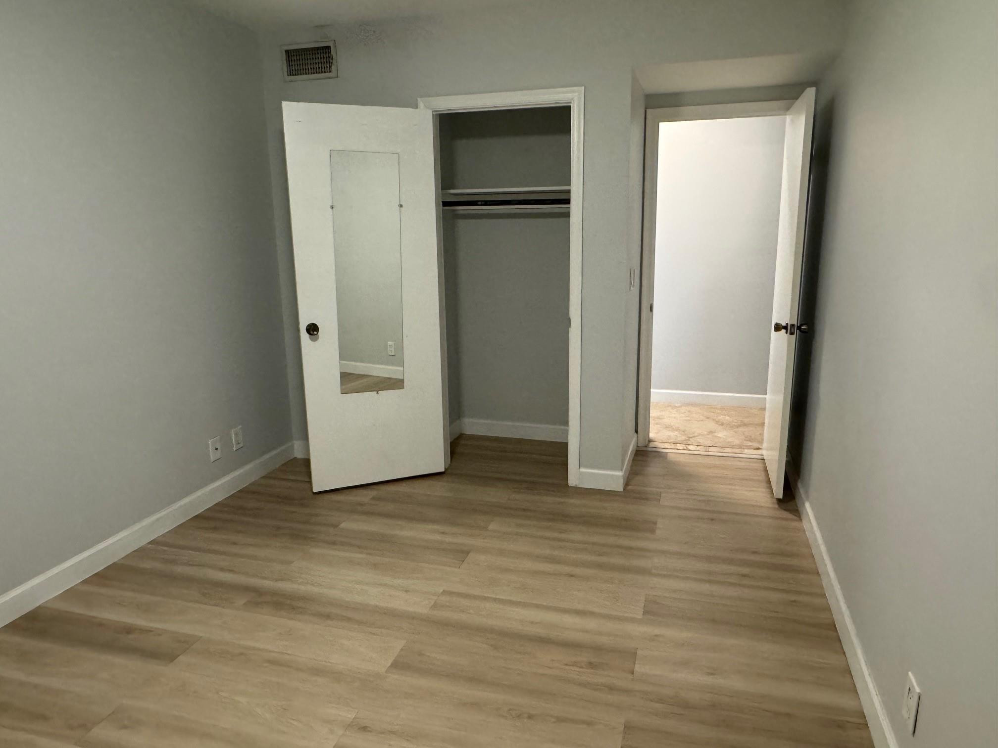 Vacant room with wood-look flooring and an open closet with a mirrored door.