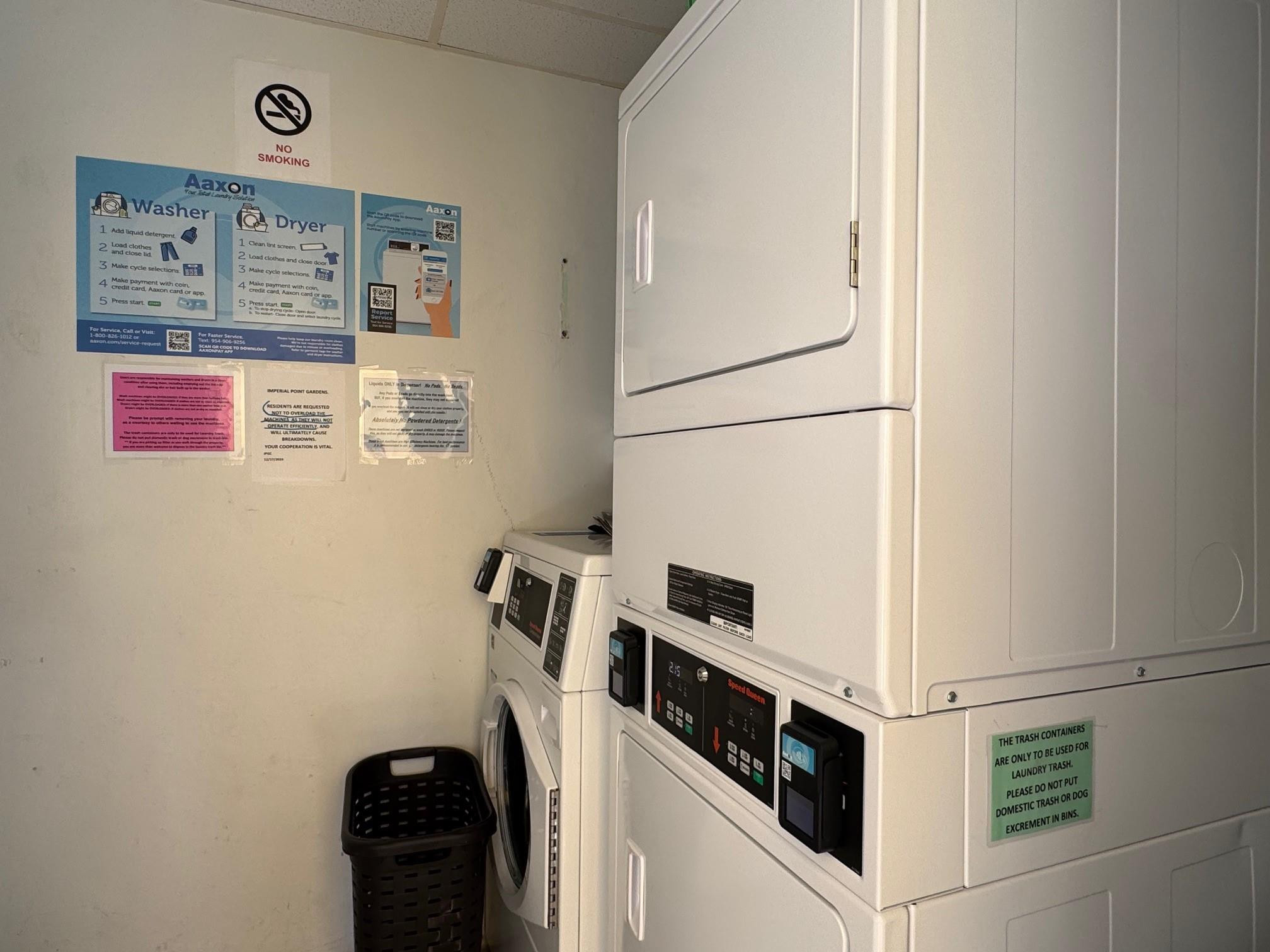 Shared laundry room with commercial stacked dryers, front-loading washers, and a black laundry basket.