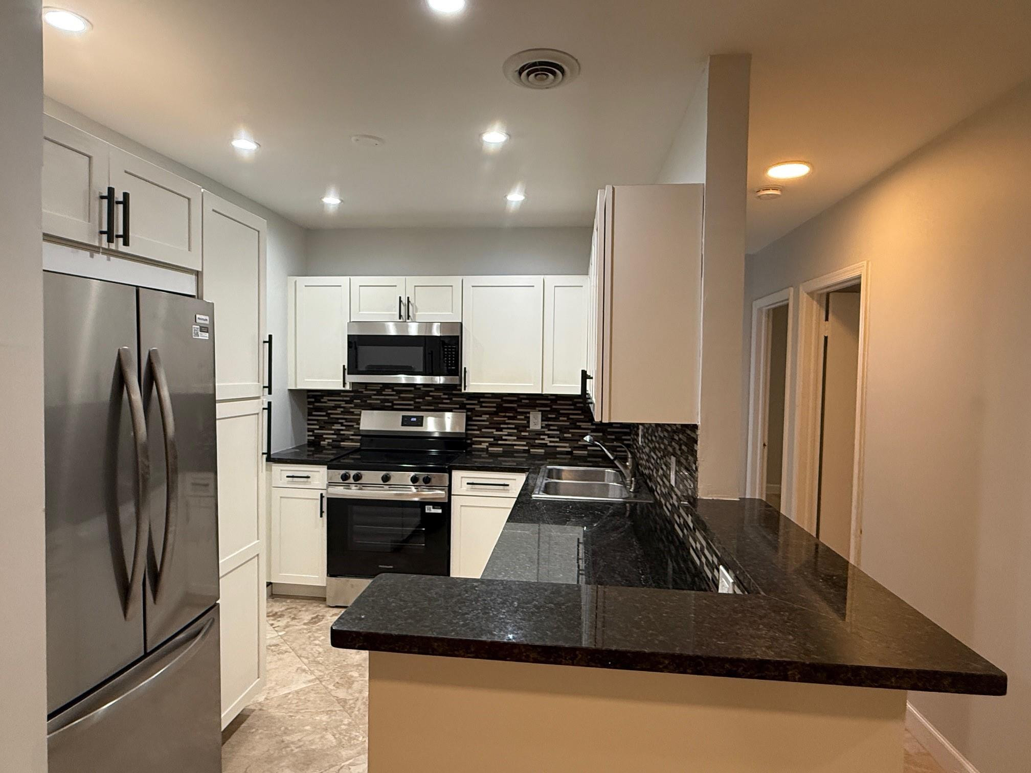 Kitchen with white cabinets, stainless steel appliances, dark granite counters, and a mosaic tile backsplash.