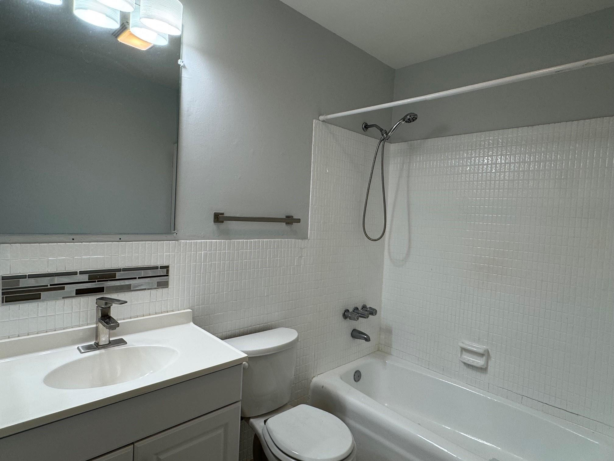 Bathroom with a white vanity, toilet, and tiled tub-shower with a handheld showerhead.