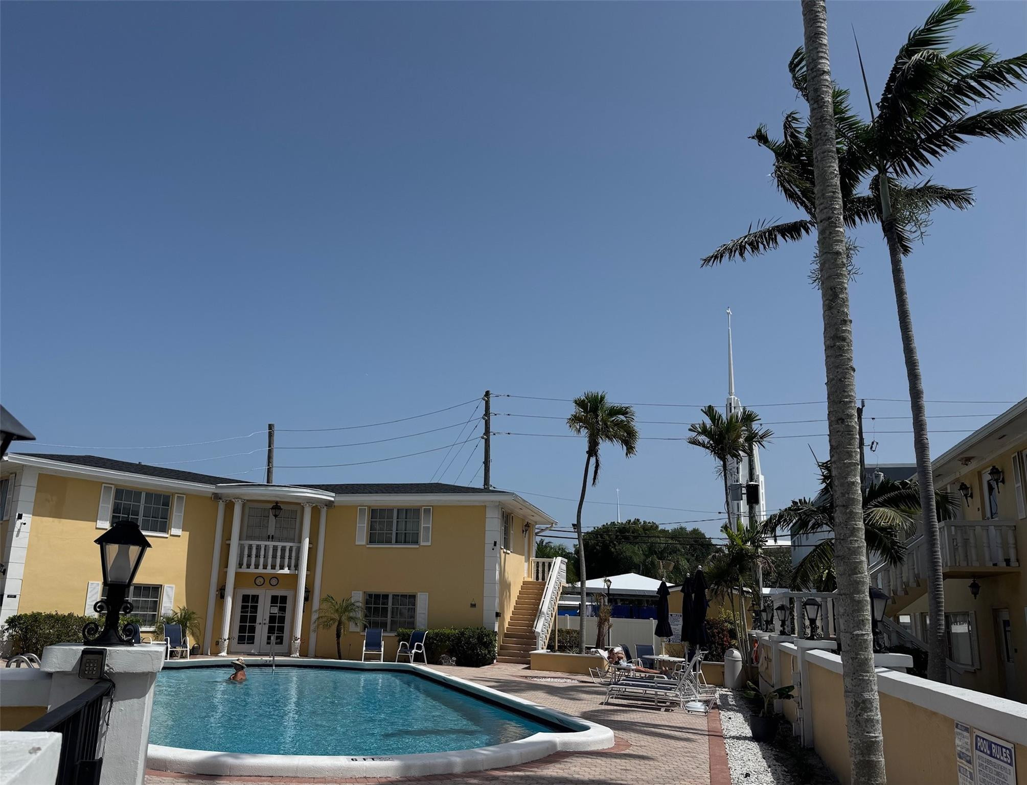 Residential courtyard pool beside a yellow building, with palm trees and poolside loungers.