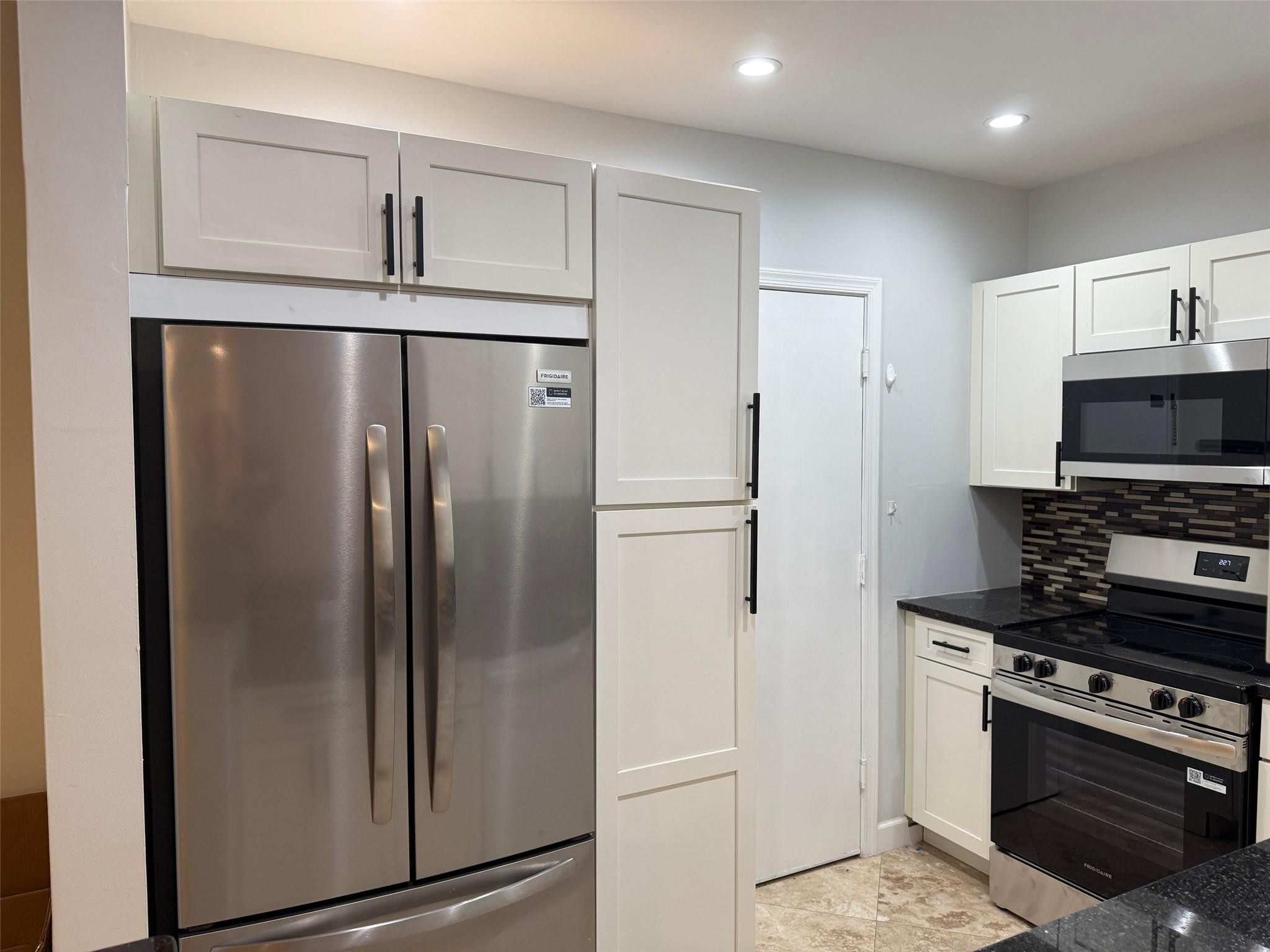 Kitchen with stainless steel appliances, white cabinets, and a dark mosaic backsplash.