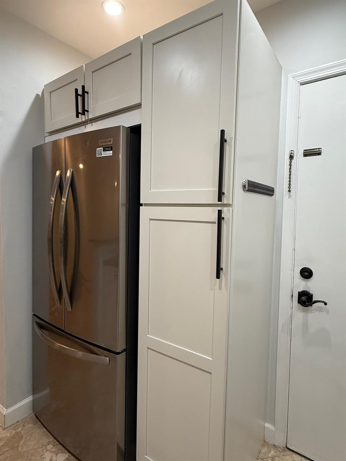 Kitchen corner with a stainless steel refrigerator, white cabinets, and an entry door.