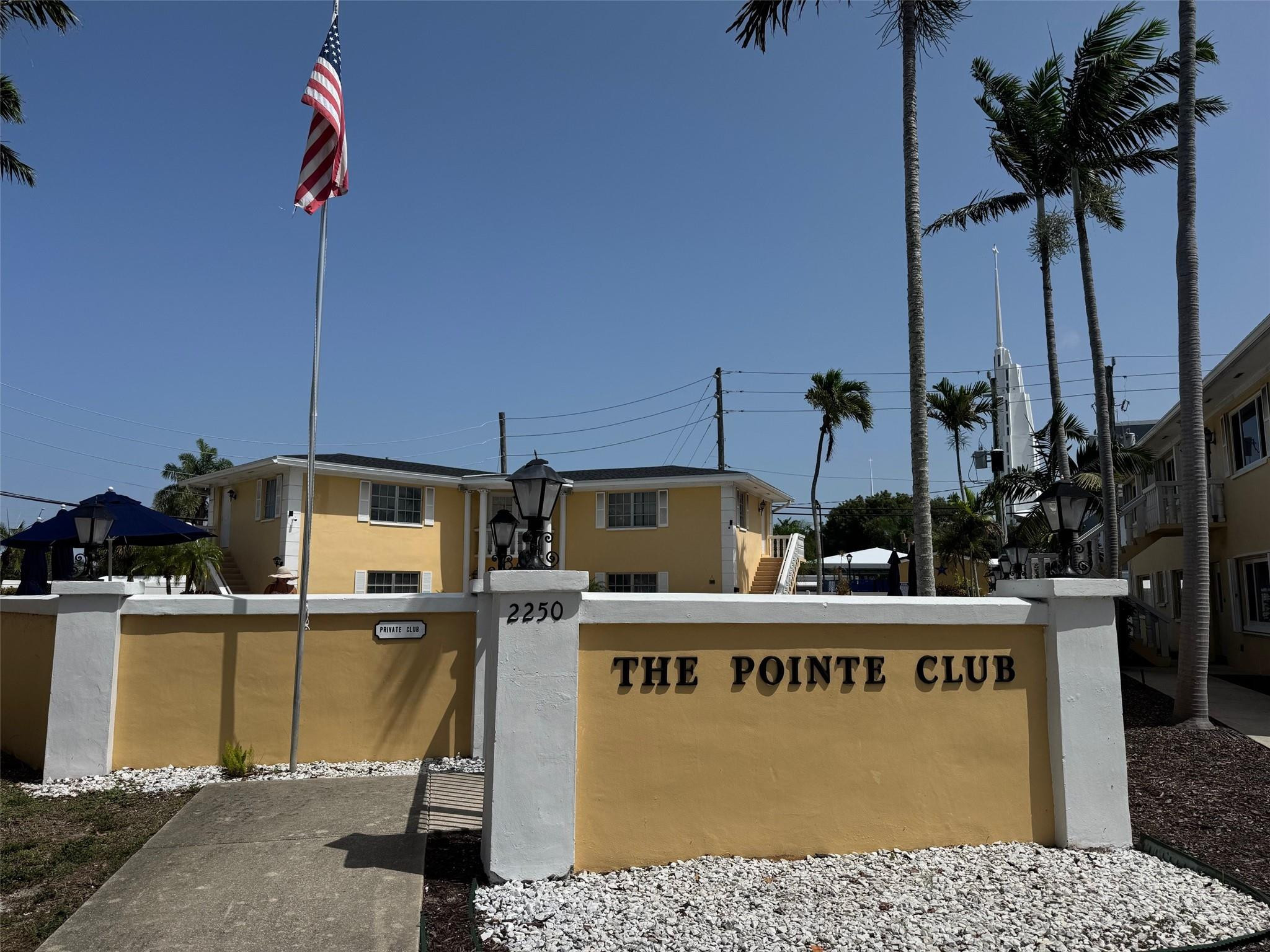 The Pointe Club entrance wall marked 2250, with a yellow building and palm trees behind it.