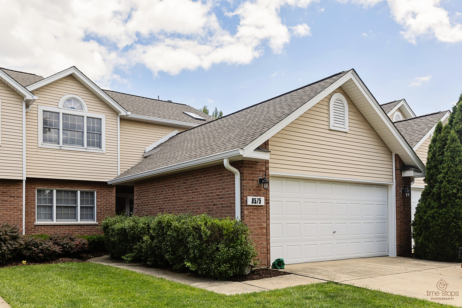 Two-story brick and beige-sided home with an attached white garage and landscaped front yard.