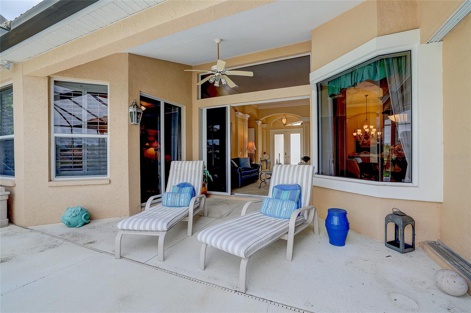 Covered patio with striped chaise lounges and a ceiling fan beside the home’s sliding glass doors.
