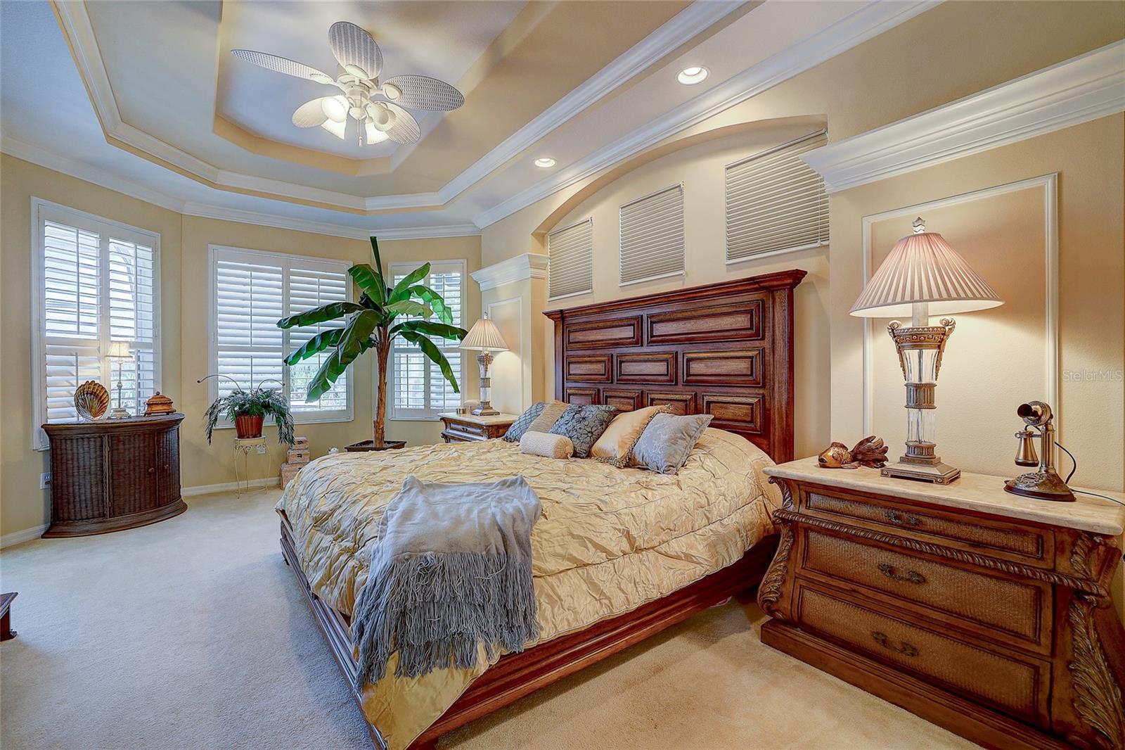 Furnished bedroom with a carved dark wood bed, plantation shutters, and a tray ceiling.
