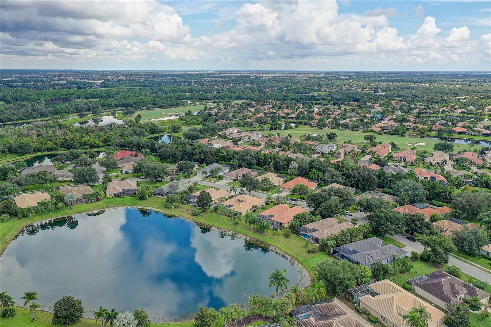 Aerial view of a residential neighborhood beside a pond, with golf-course greens and screened pools.