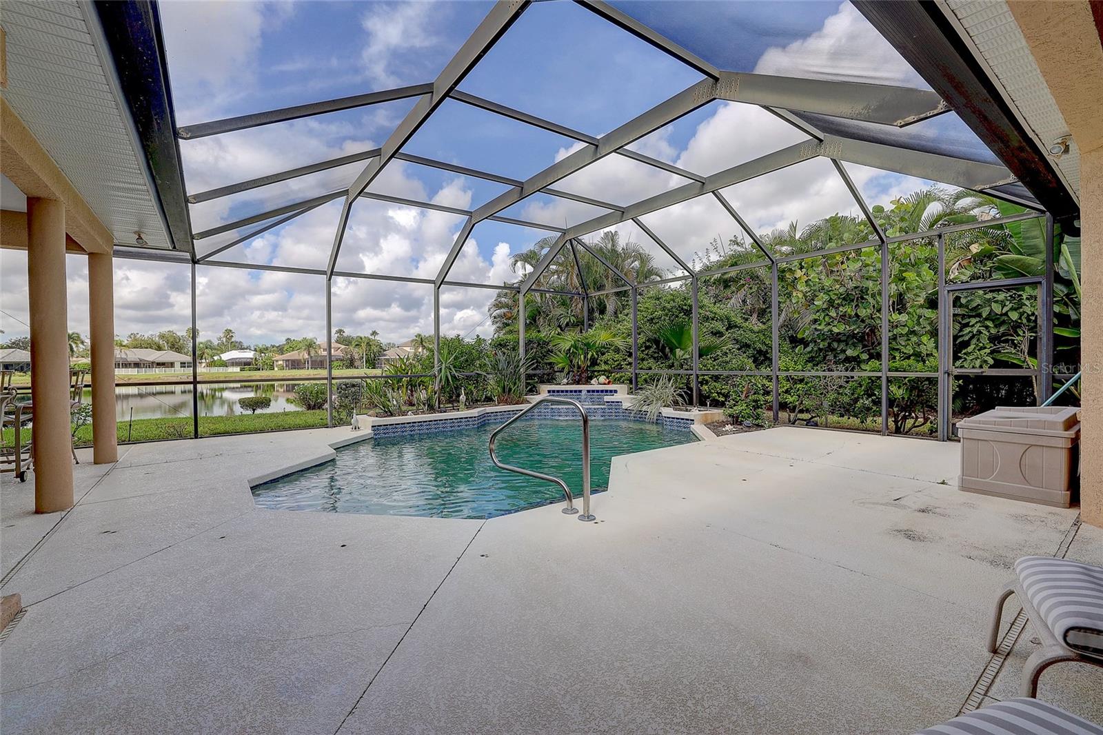 Backyard pool beneath a screened lanai, with tropical landscaping and a pond beyond.