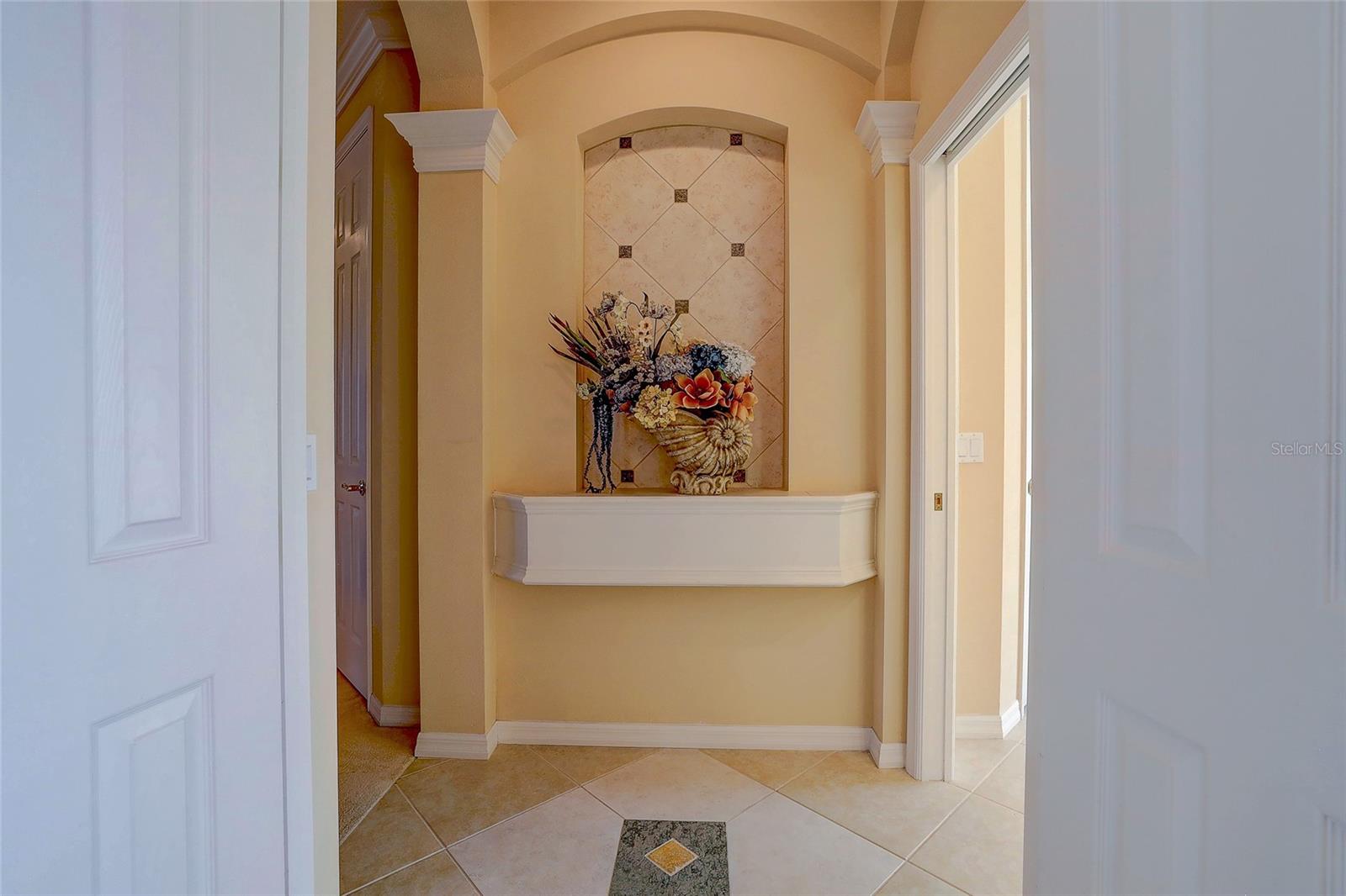 Foyer with a tiled floor and arched decorative niche above a white display shelf.