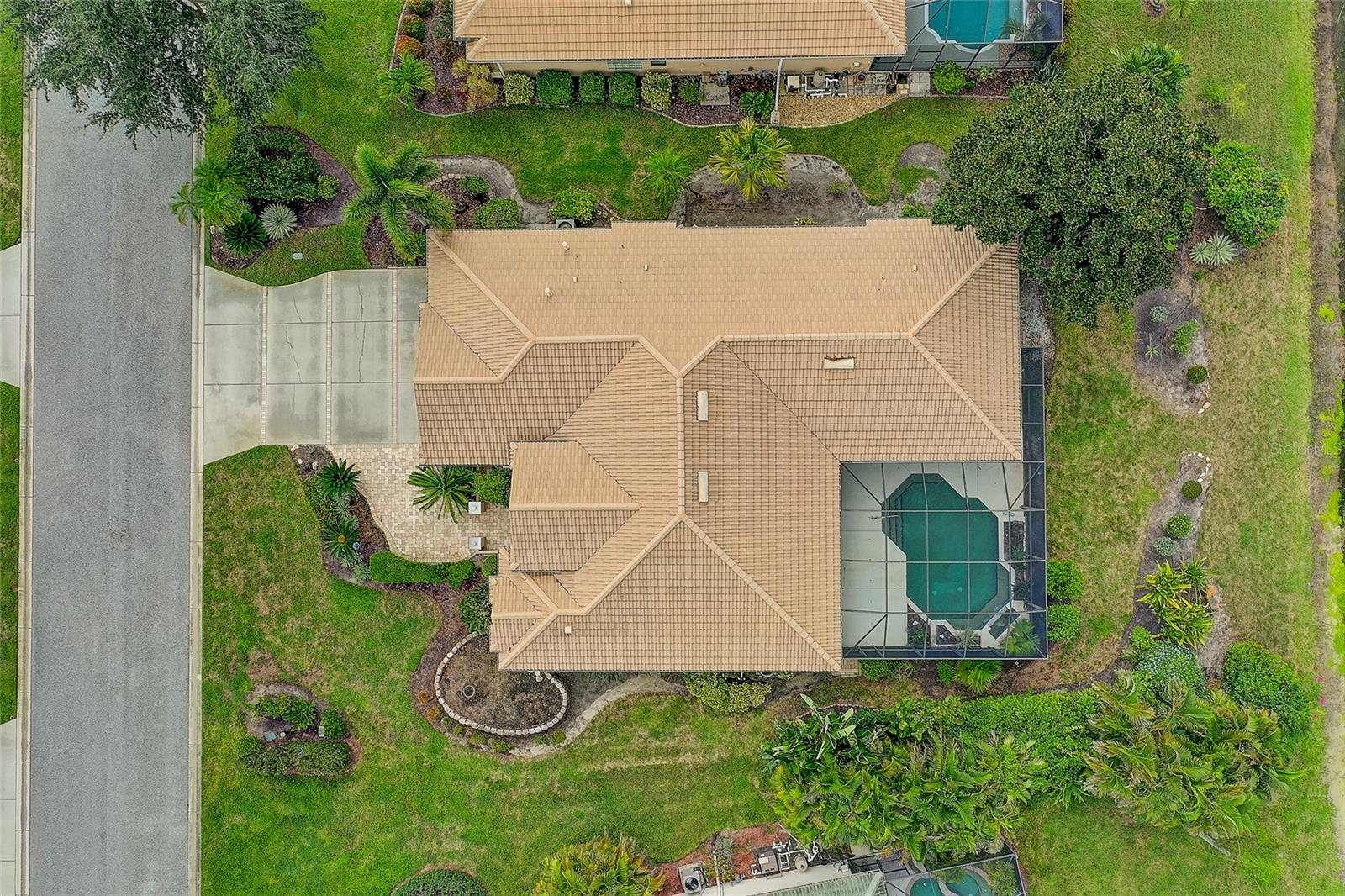 Aerial view of a landscaped home with a terracotta tile roof and screened pool.