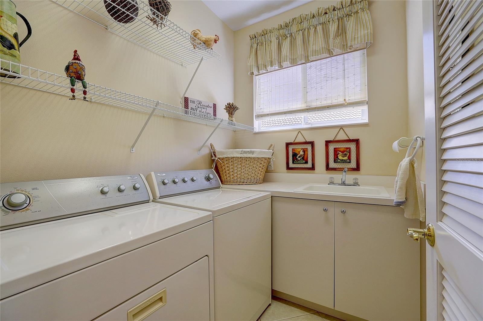 Laundry room with washer and dryer, utility sink, wire shelving, and a window with blinds.