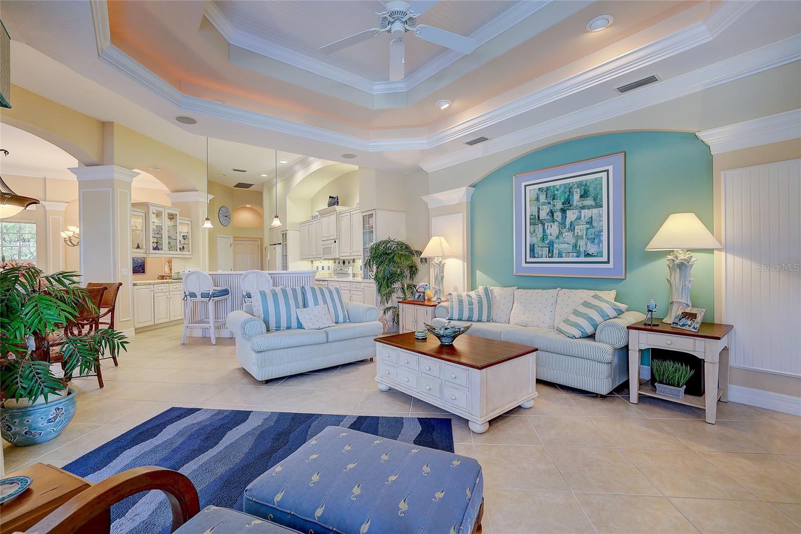 Living room with striped sofas, a turquoise accent wall, and a tray ceiling, open to the kitchen.