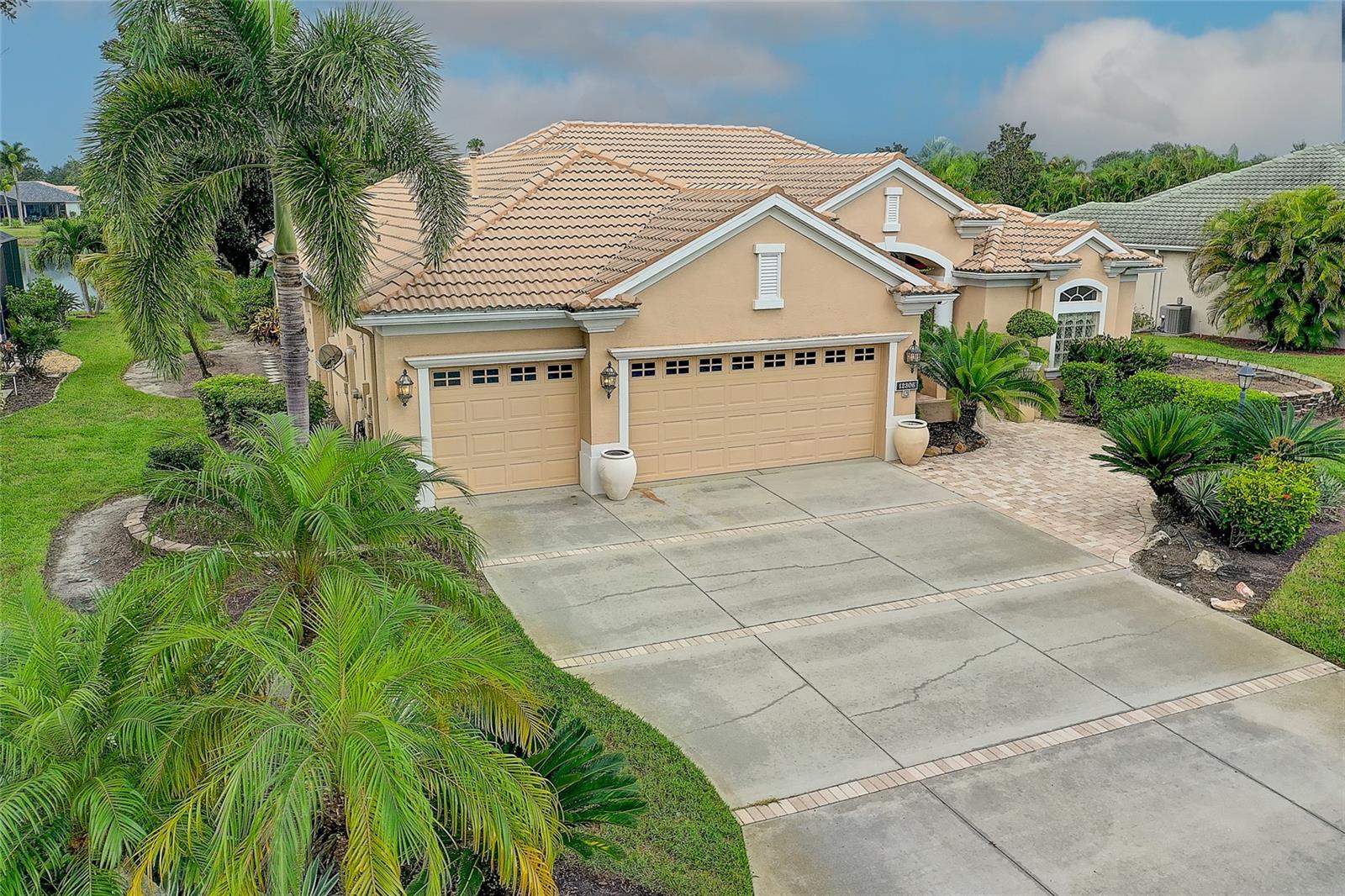 Tan stucco home with a tile roof and three-car garage, framed by palms beside a canal.