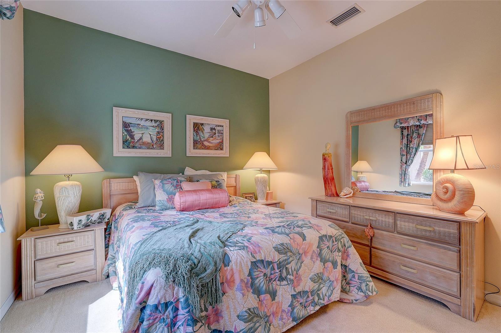 Bedroom with tropical floral bedding, green accent wall, and matching light wood furniture.