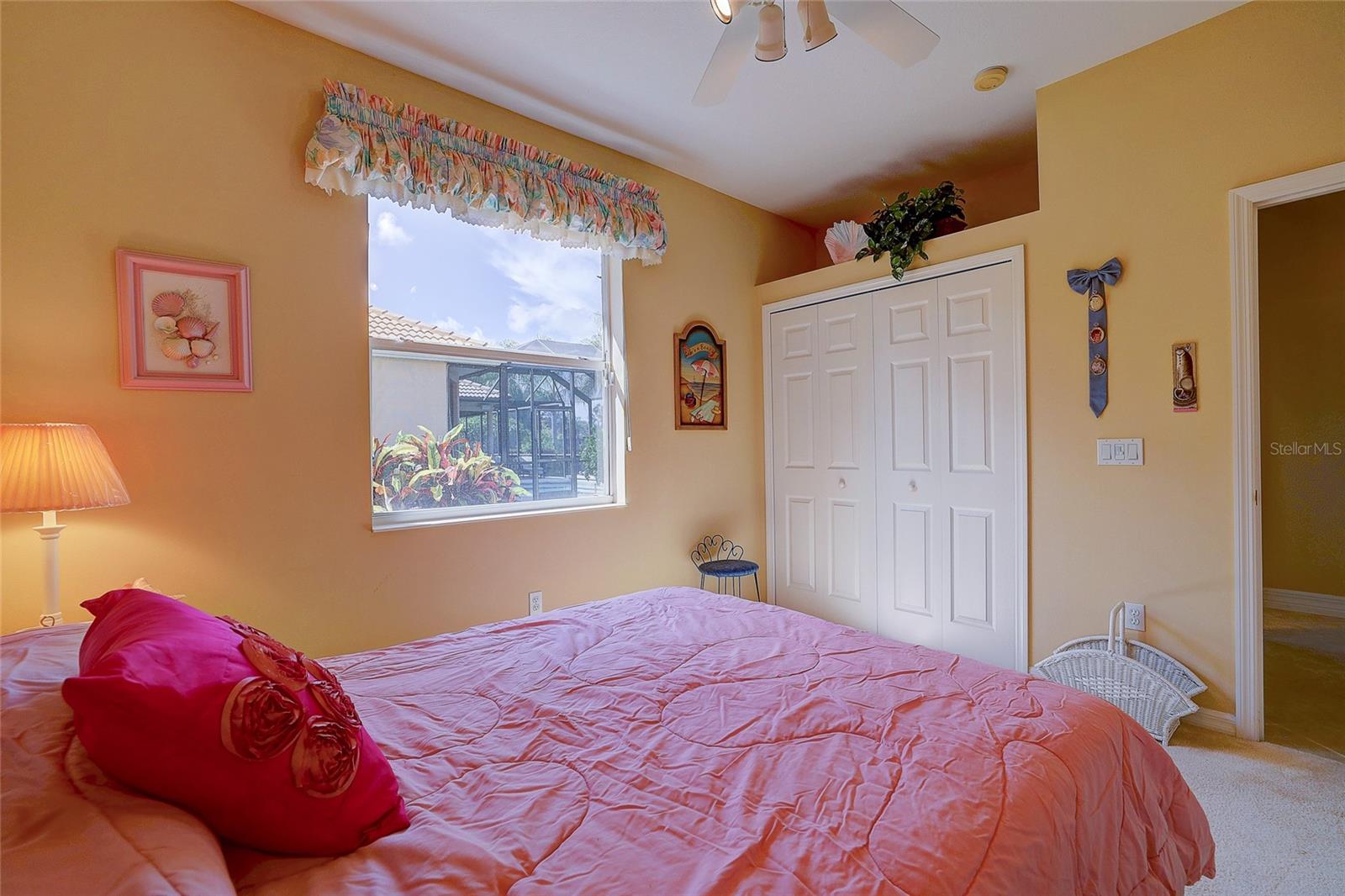 Bedroom with a pink quilted bed, white closet doors, and a window overlooking a screened lanai.