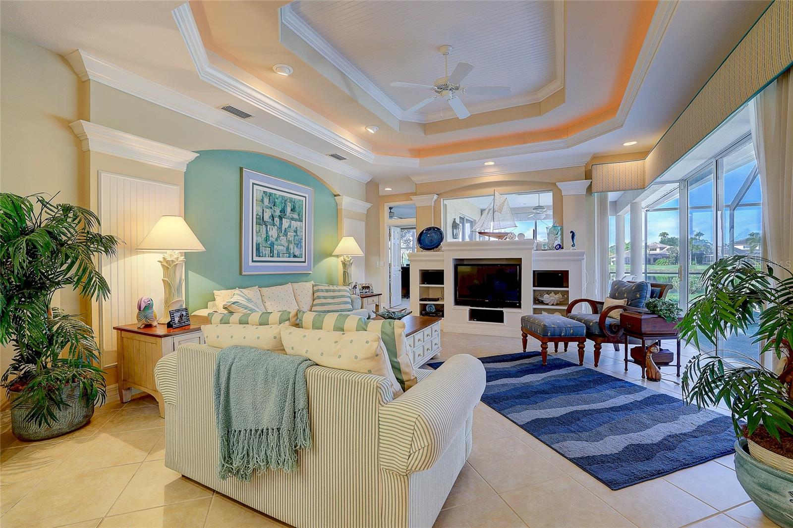 Living room with a tray ceiling, fireplace, striped sofas, and large windows overlooking a lake.