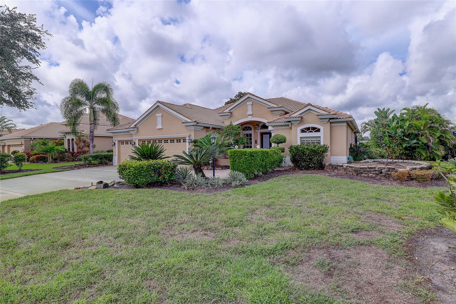 Tan stucco home with a tiled roof, three-car garage, arched entry, and landscaped front lawn.