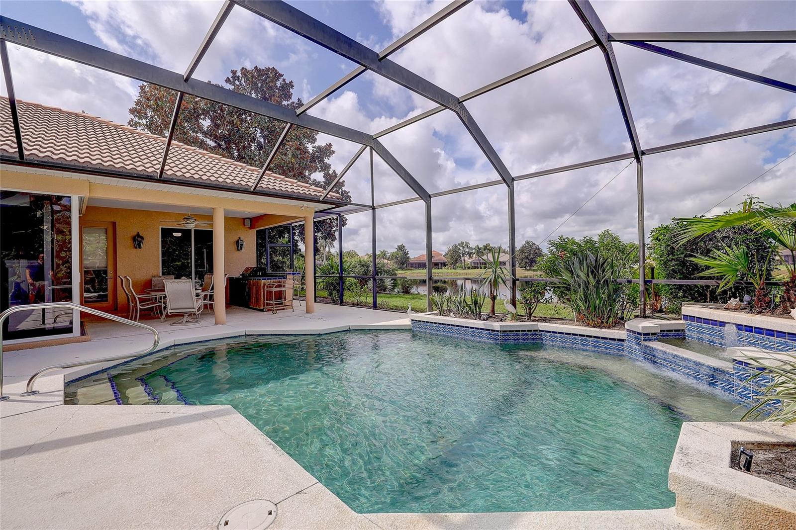 Screened backyard pool and raised spa beside a covered patio, with a lake beyond.