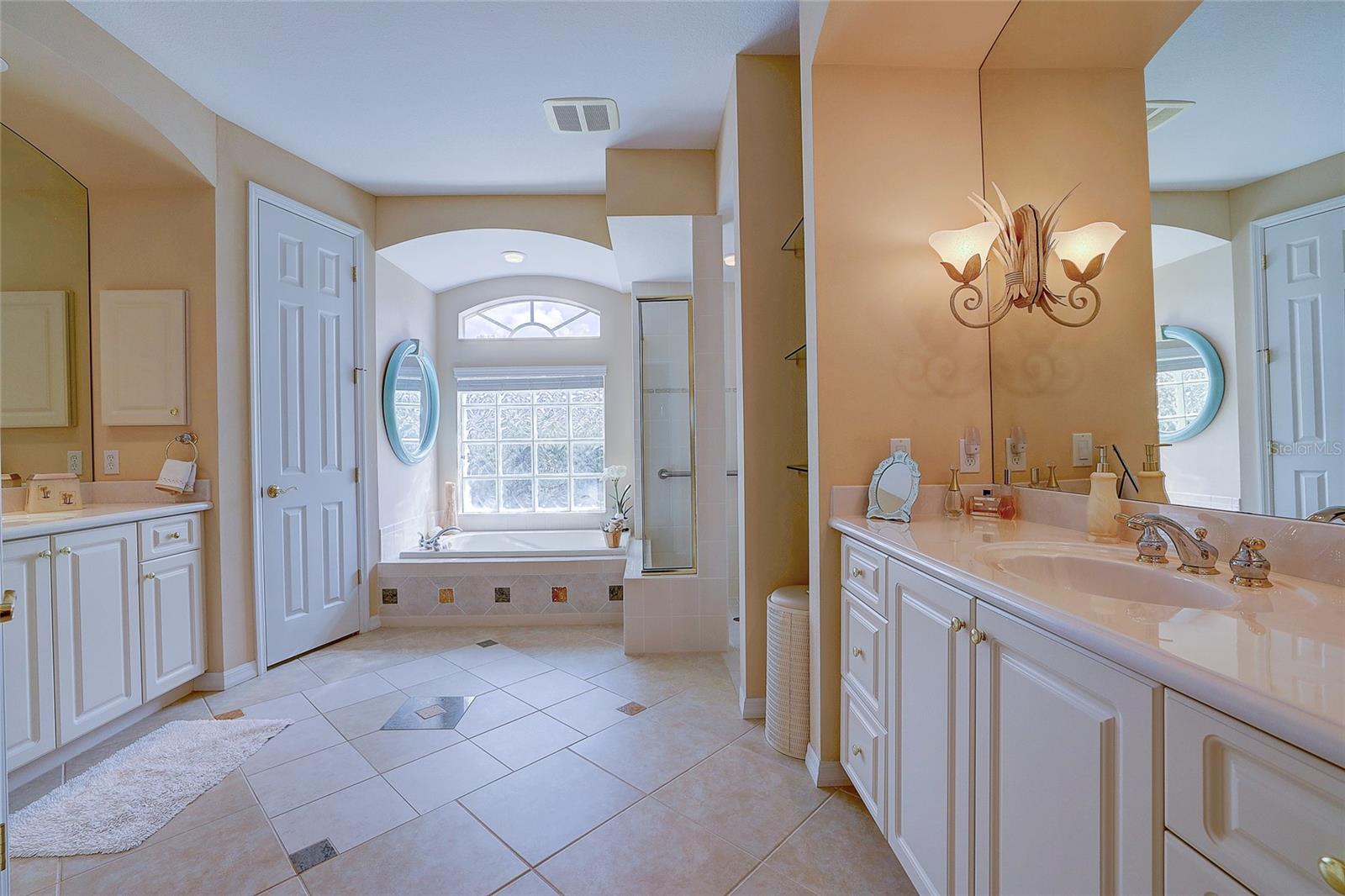 Bathroom with a soaking tub beneath an arched window, glass shower, and white double vanities.