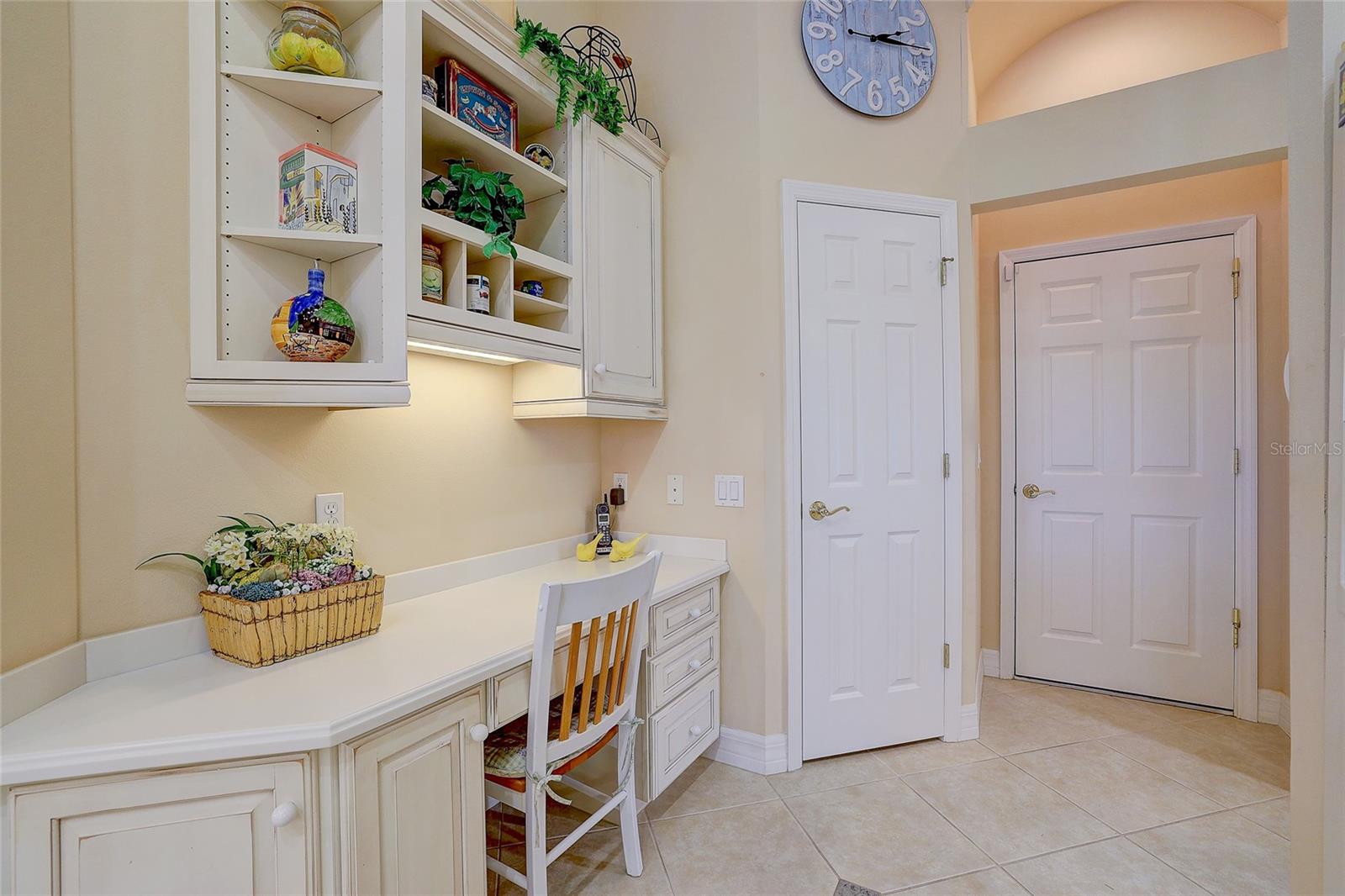 Built-in home office with white cabinetry, open display shelves, and a chair beside two doors.