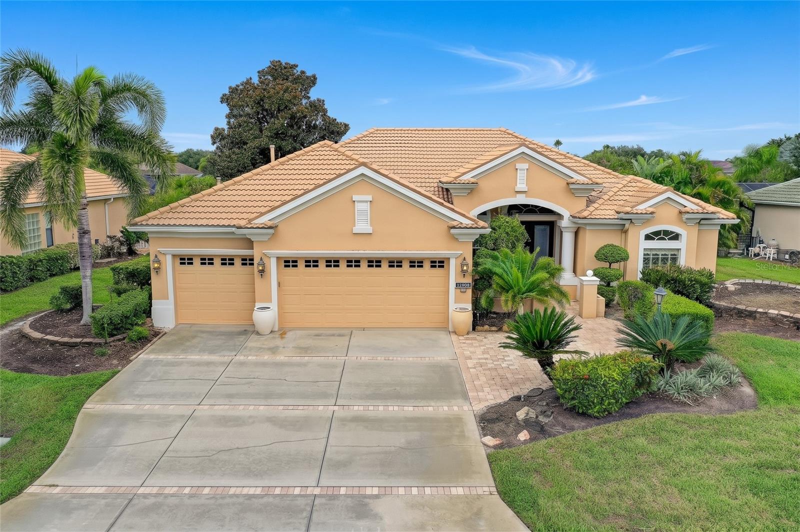 Peach stucco home with a terracotta tile roof, three-car garage, and tropical landscaping.