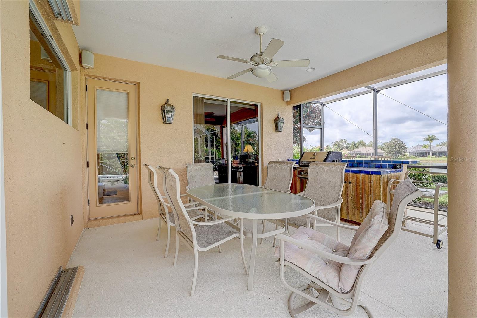 Screened lanai with outdoor dining set, built-in grill, and blue-tiled pool edge.