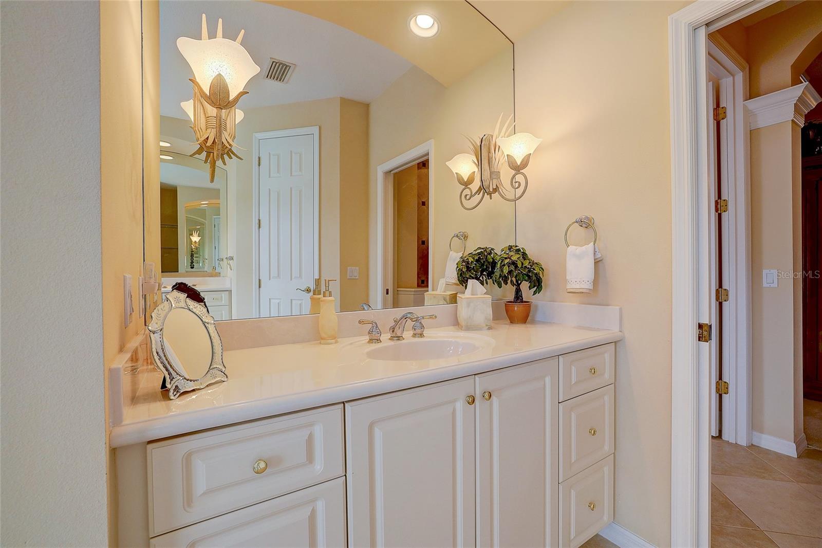Bathroom vanity with white cabinetry, a long countertop, large mirror, and decorative sconces.