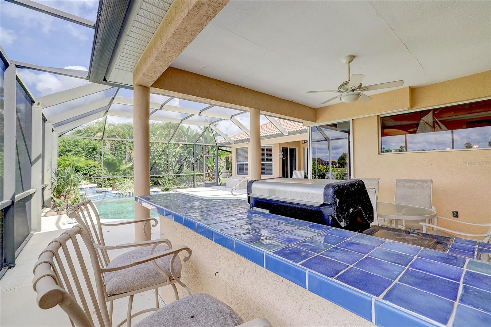 Covered outdoor kitchen with a blue-tiled bar and grill beside a screened pool.