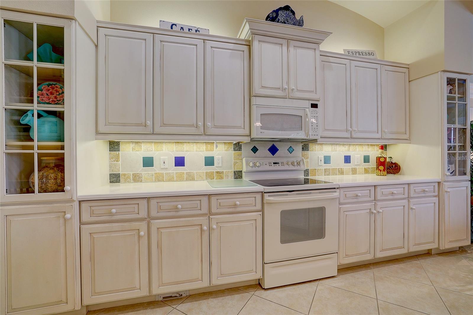 Kitchen with cream cabinetry, colorful tiled backsplash, and white range and microwave.