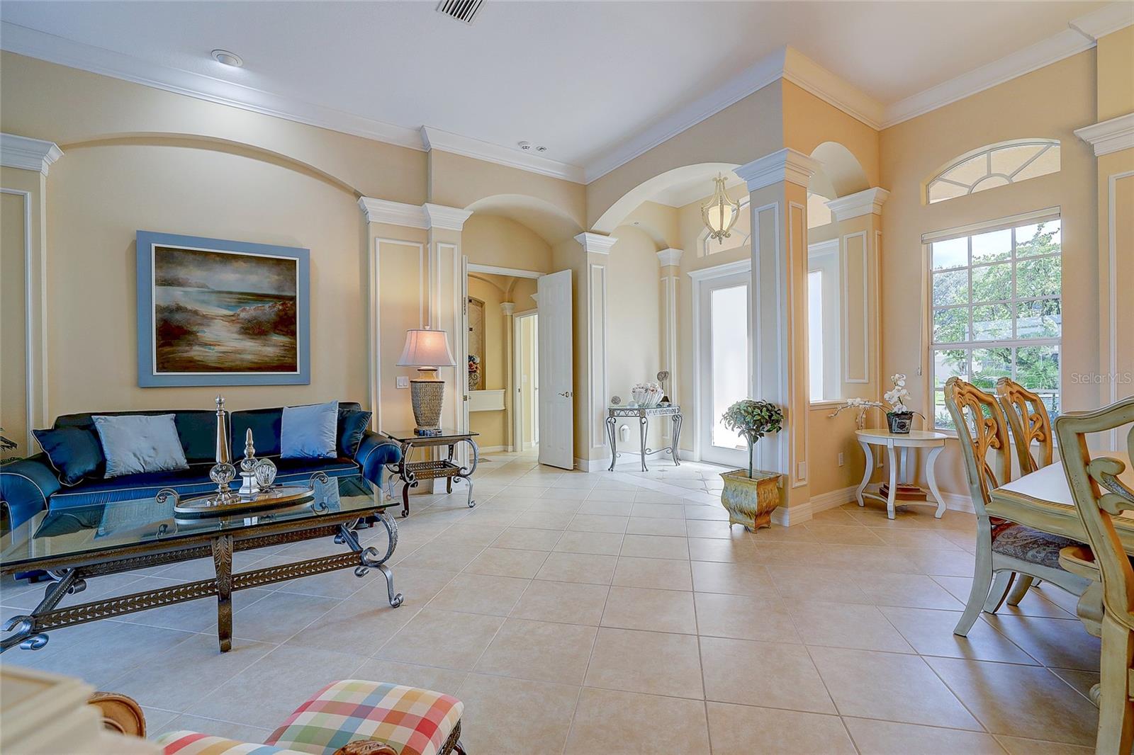 Furnished living room with a blue sofa, tiled floors, arched openings, and tall windows.
