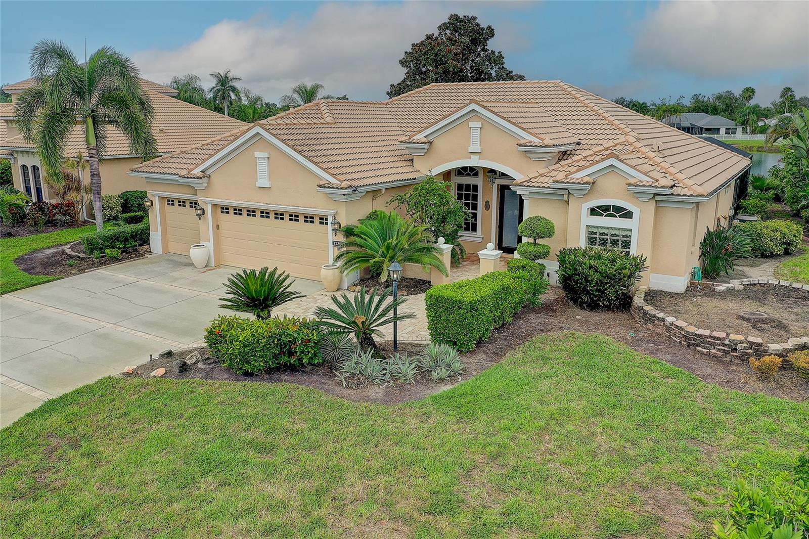 Peach stucco home with a terracotta tile roof, three-car garage, and landscaped front yard.