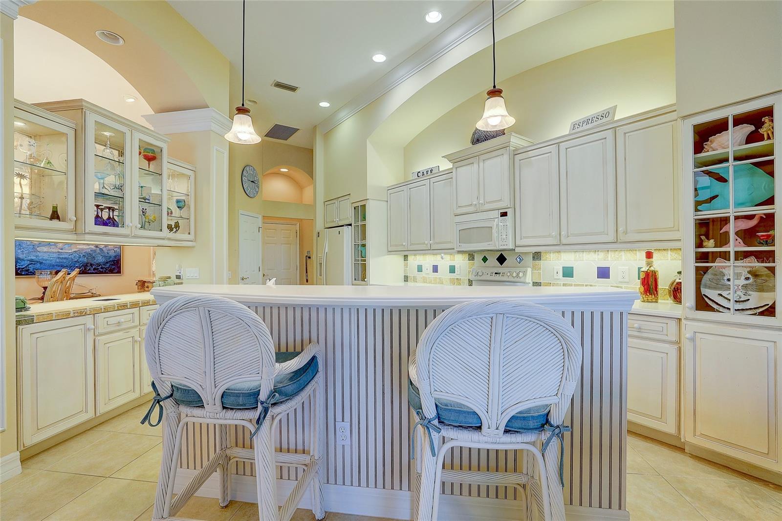 Kitchen with white cabinetry, glass-front displays, and a large island with two wicker stools.