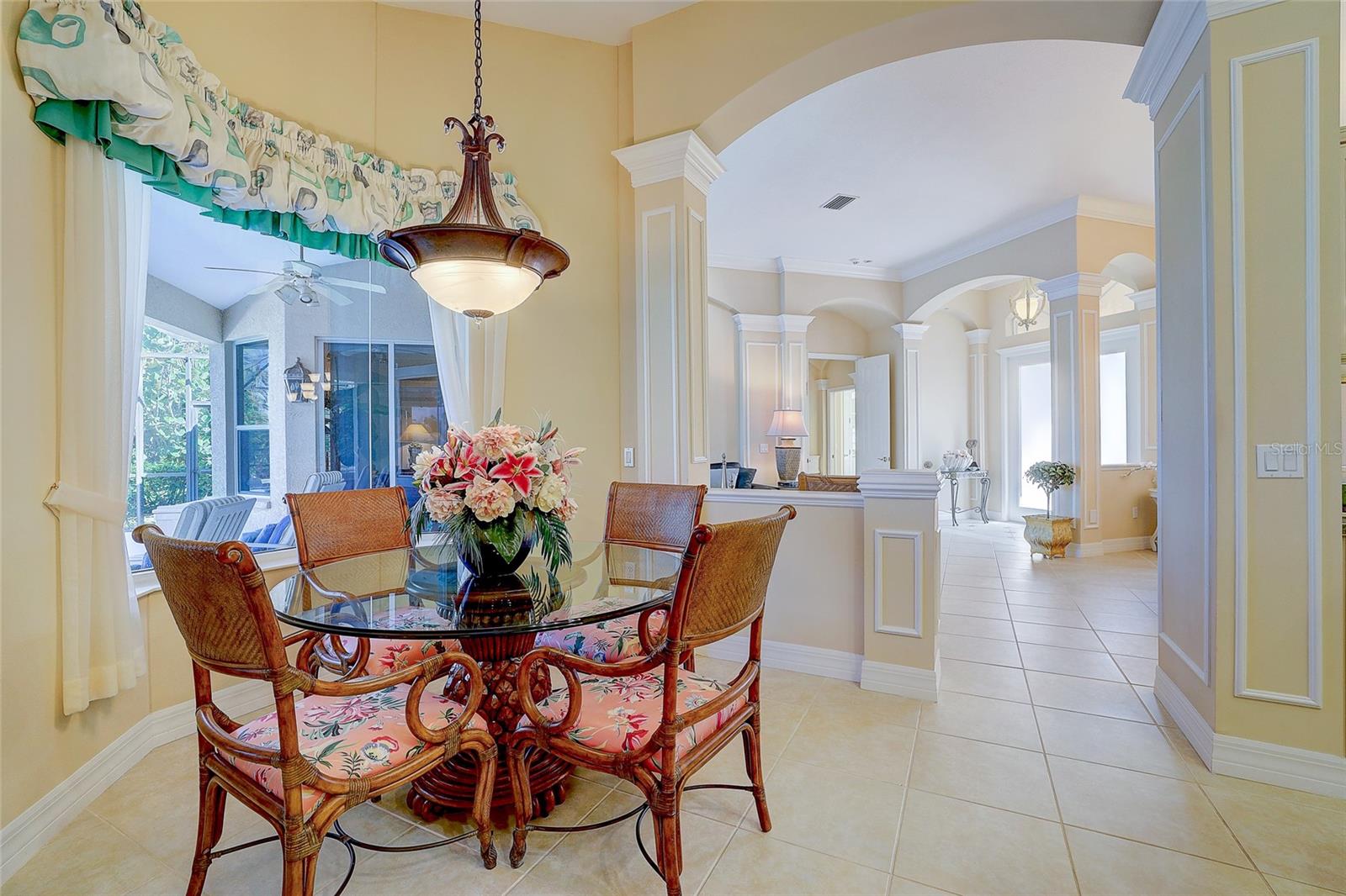 Dining room with ornate chairs, a glass table, floral centerpiece, and arched openings.