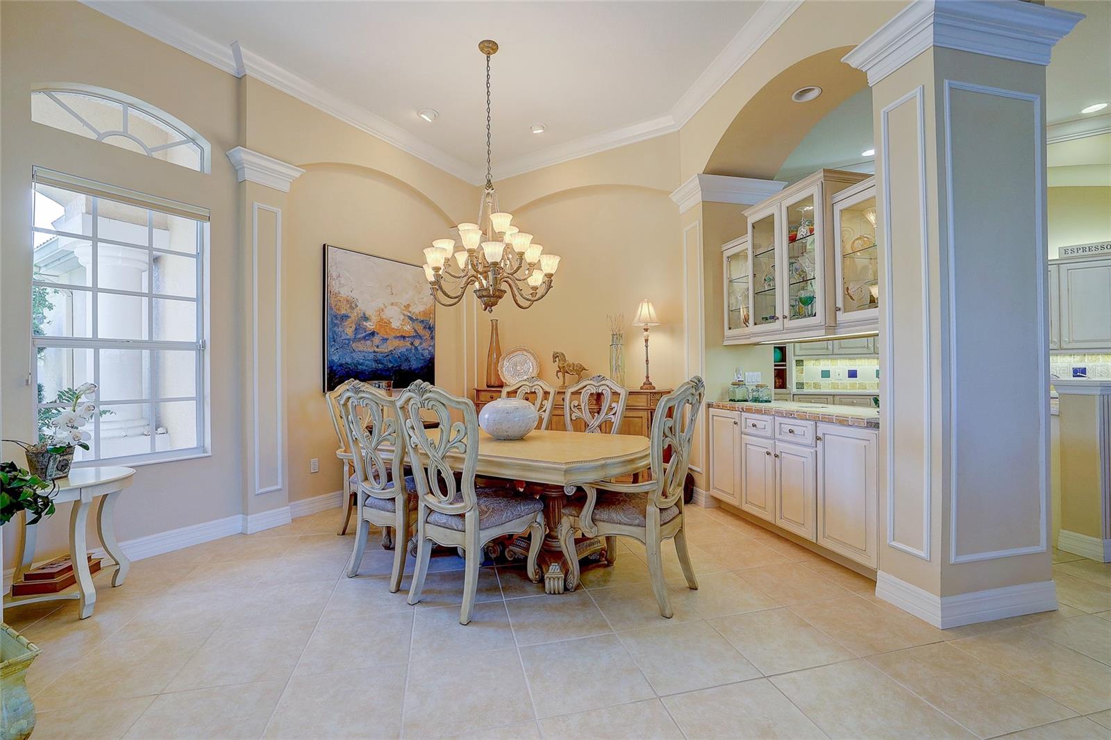 Dining room with an ornate table, chandelier, arched details, and built-in glass-front cabinets.