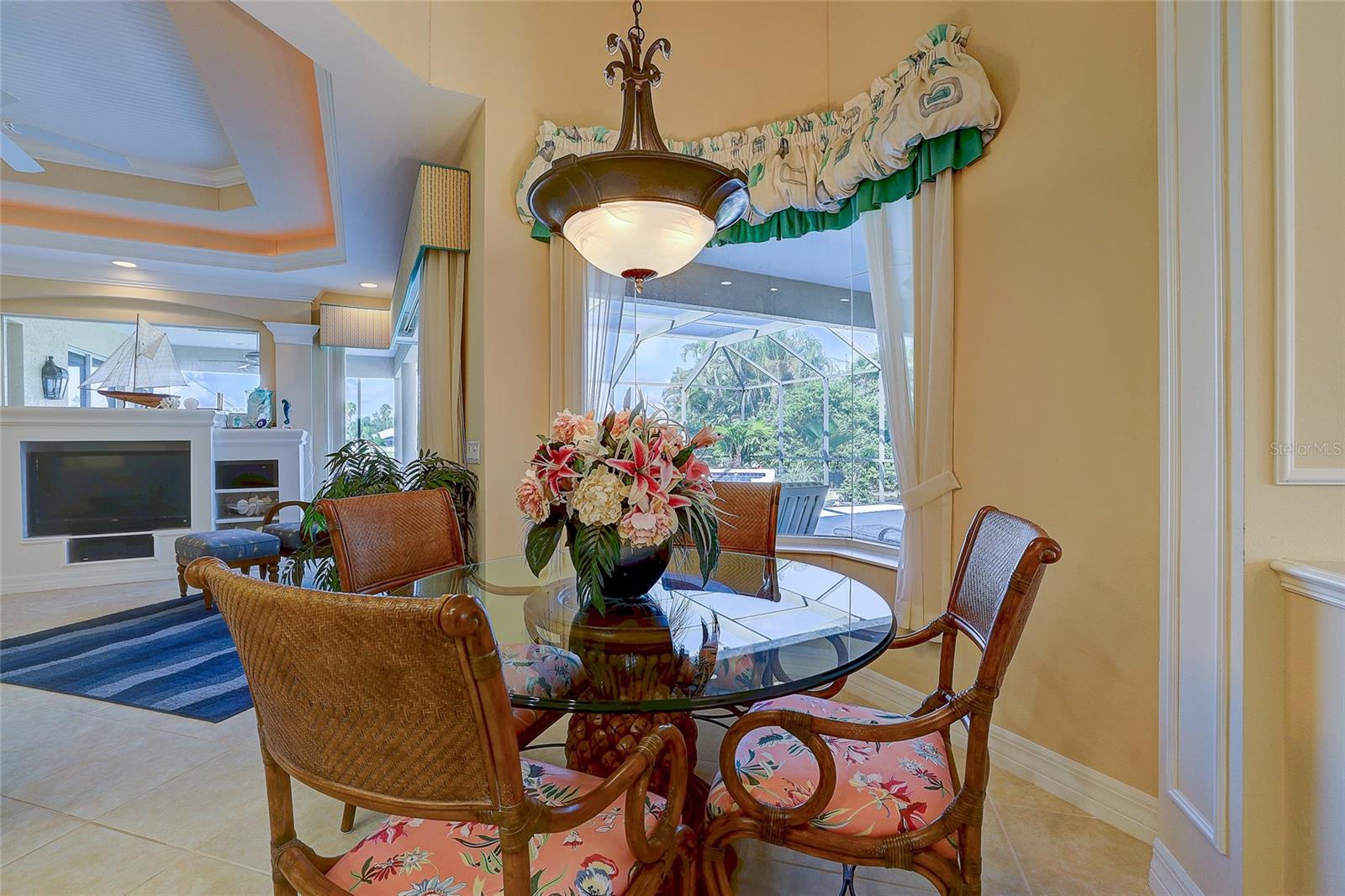 Dining area with a glass-top table and wicker chairs beside a window overlooking a screened lanai.