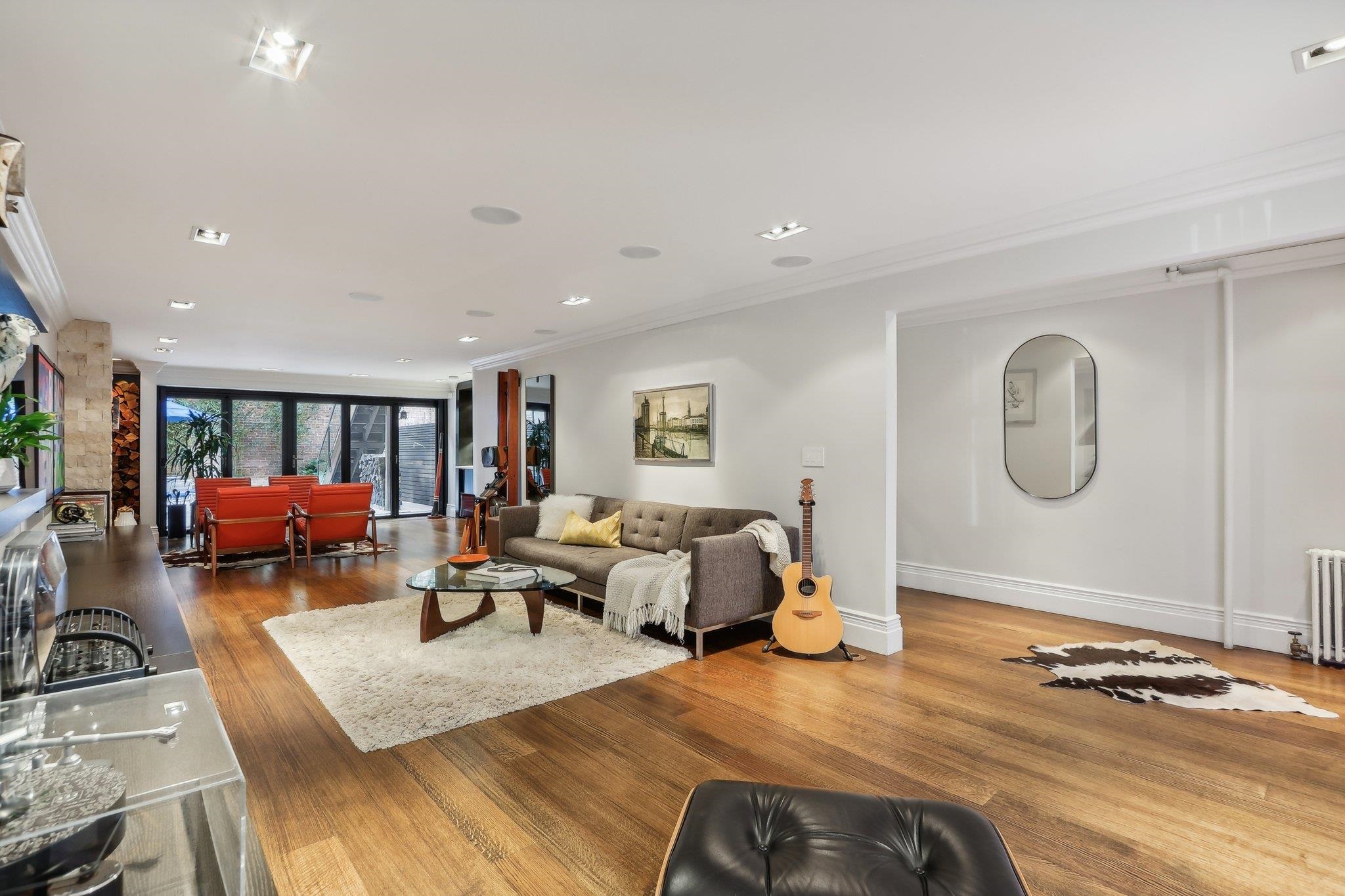 Open-plan living room with wood floors, gray sofa, red chairs, and large glass doors.