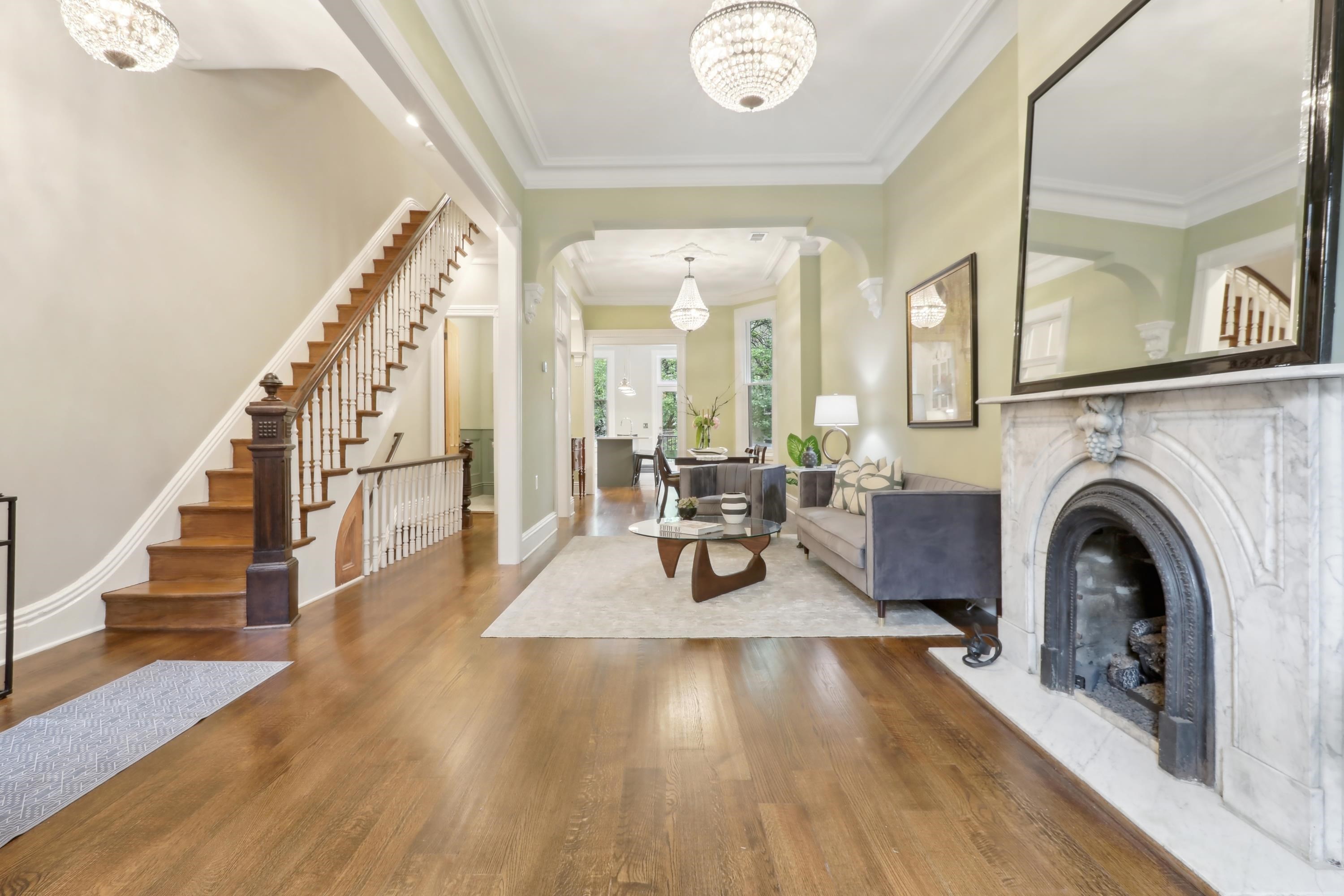Living room with hardwood floors, a marble fireplace, a staircase, and crystal chandeliers.