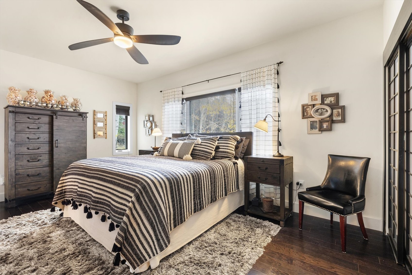 Bedroom with a striped quilt on the bed, dark wood furniture, and a black leather chair.