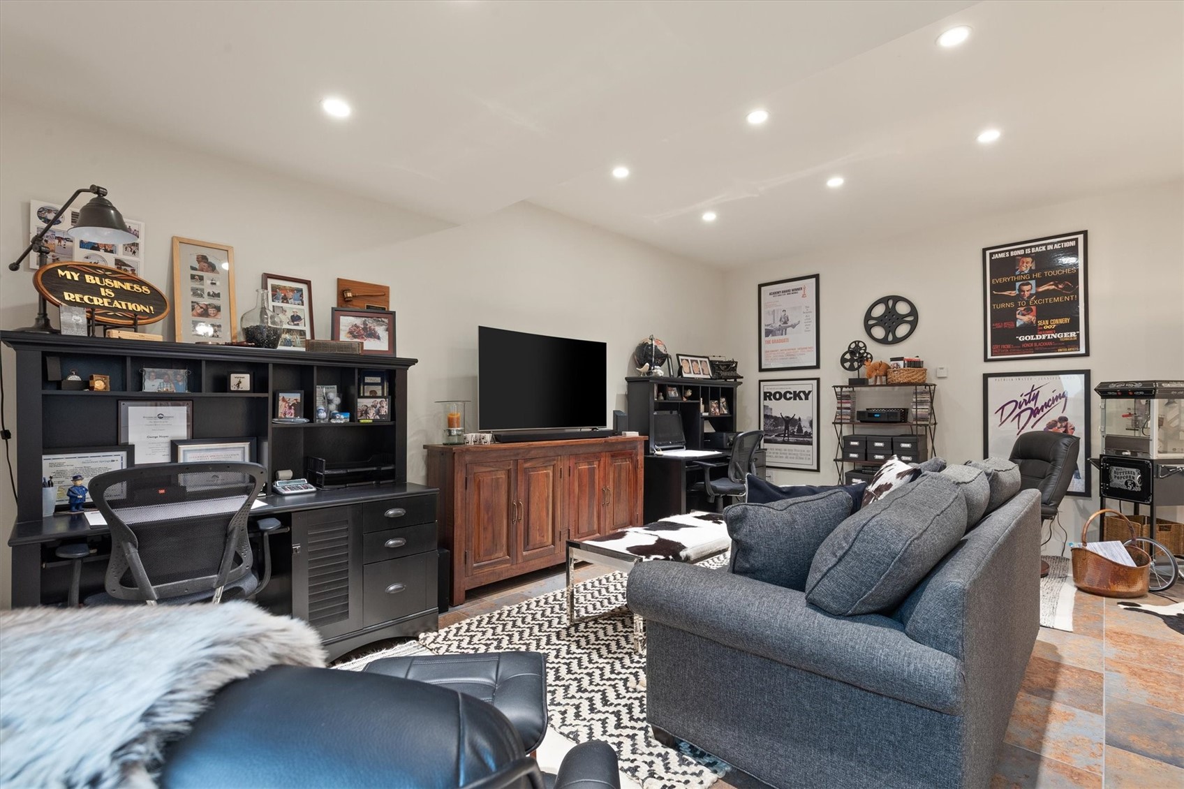 Furnished home theater and office with a large TV, gray sofa, movie posters, and a popcorn machine.