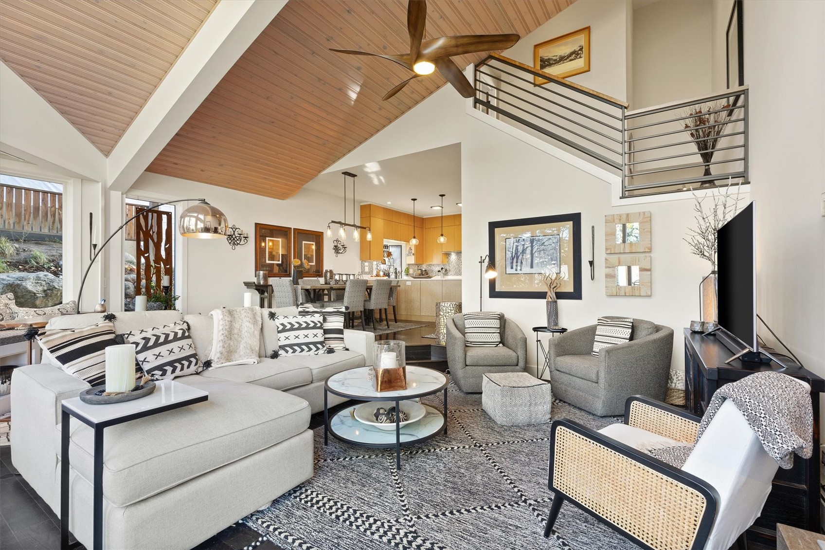 Open-plan living room with vaulted wood ceiling, sectional seating, and kitchen and dining area beyond.