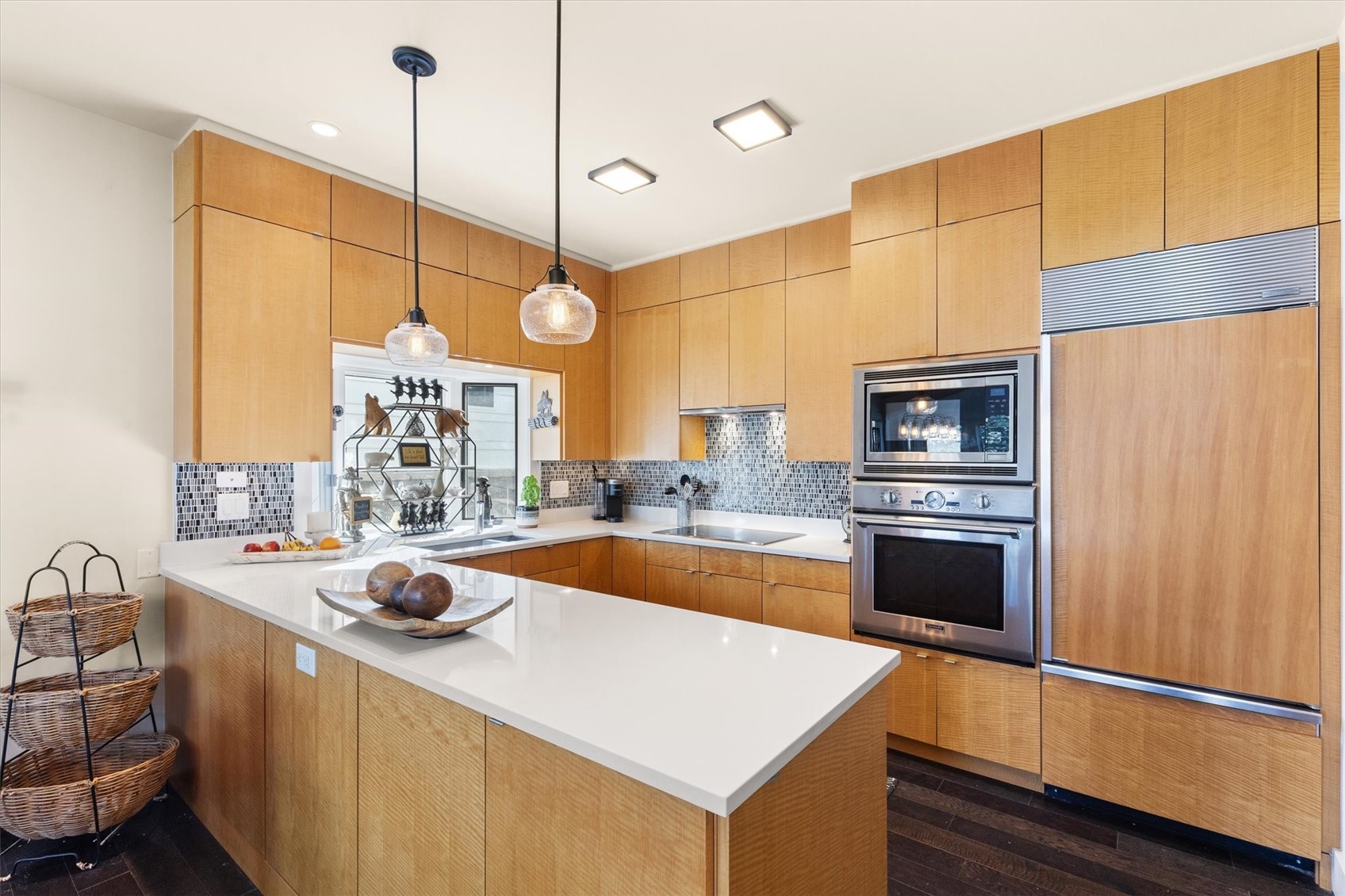 Modern kitchen with honey-toned wood cabinets, white island, mosaic backsplash, and built-in stainless steel appliances.