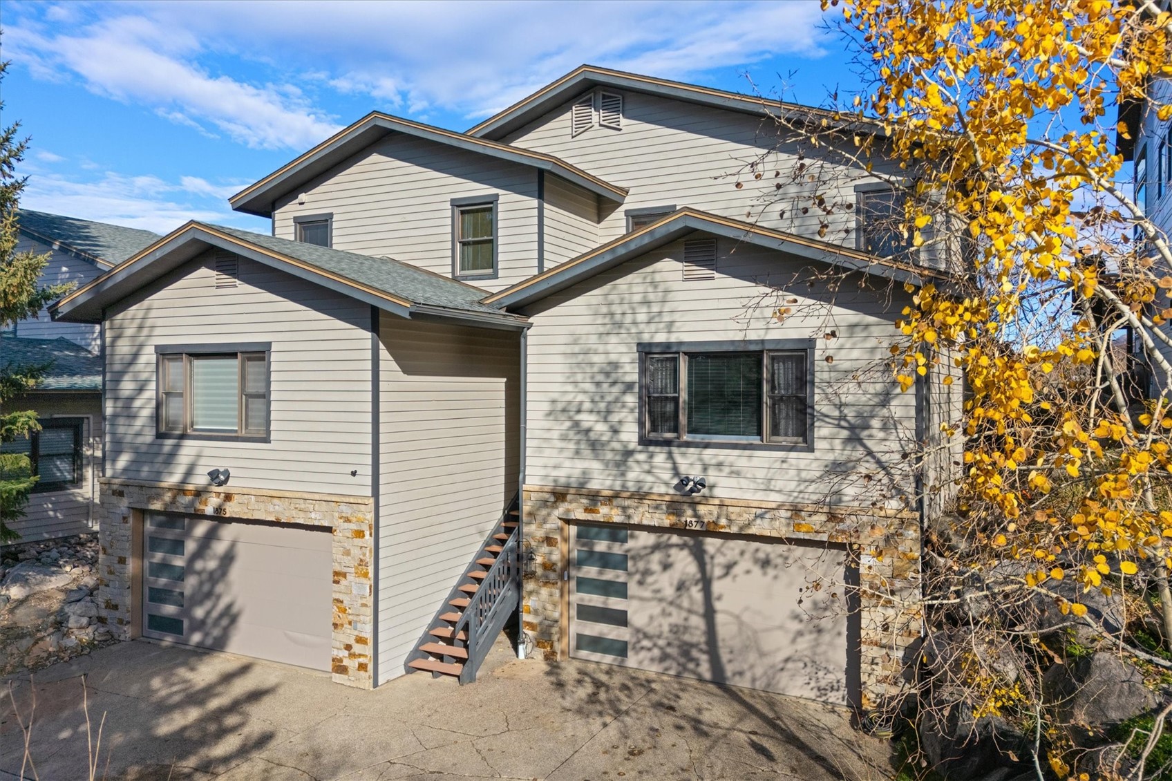Gray two-story home with stone-trimmed garage doors and golden autumn leaves.