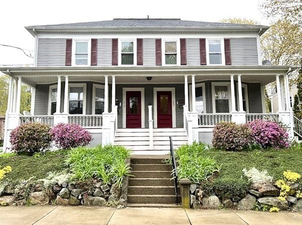White two-story home with a broad porch, red doors, and stone-edged garden steps.