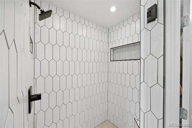 Walk-in shower with white hexagonal tile, black fixtures, and a recessed wall niche.