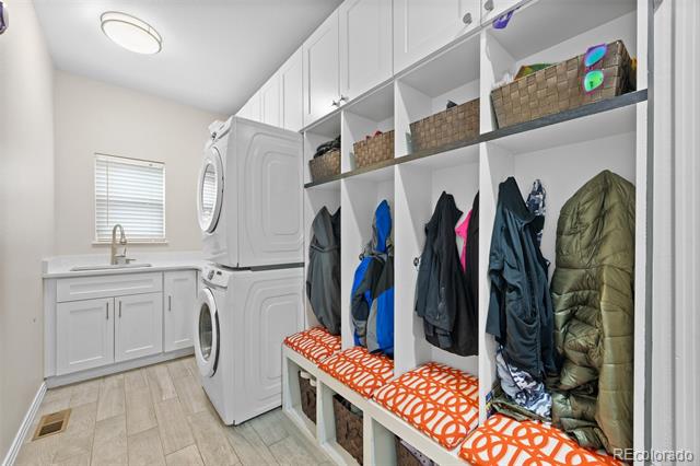 Laundry room with stacked washer and dryer, utility sink, and built-in coat cubbies.