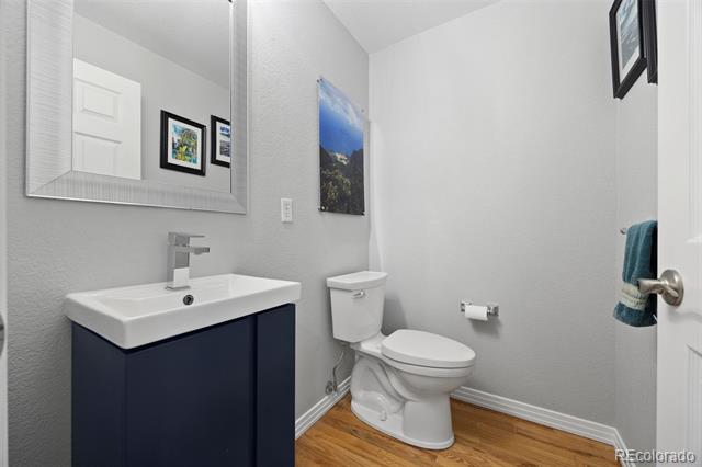 Bathroom with a navy vanity, white sink and toilet, wood-look flooring, and teal towel.