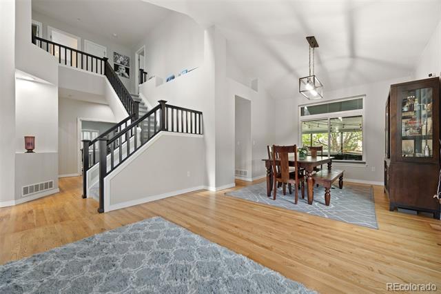 Dining area with a large window beside a black-railed staircase and hardwood floors.