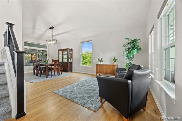 Open living and dining room with tall windows, light wood floors, and black leather chairs.